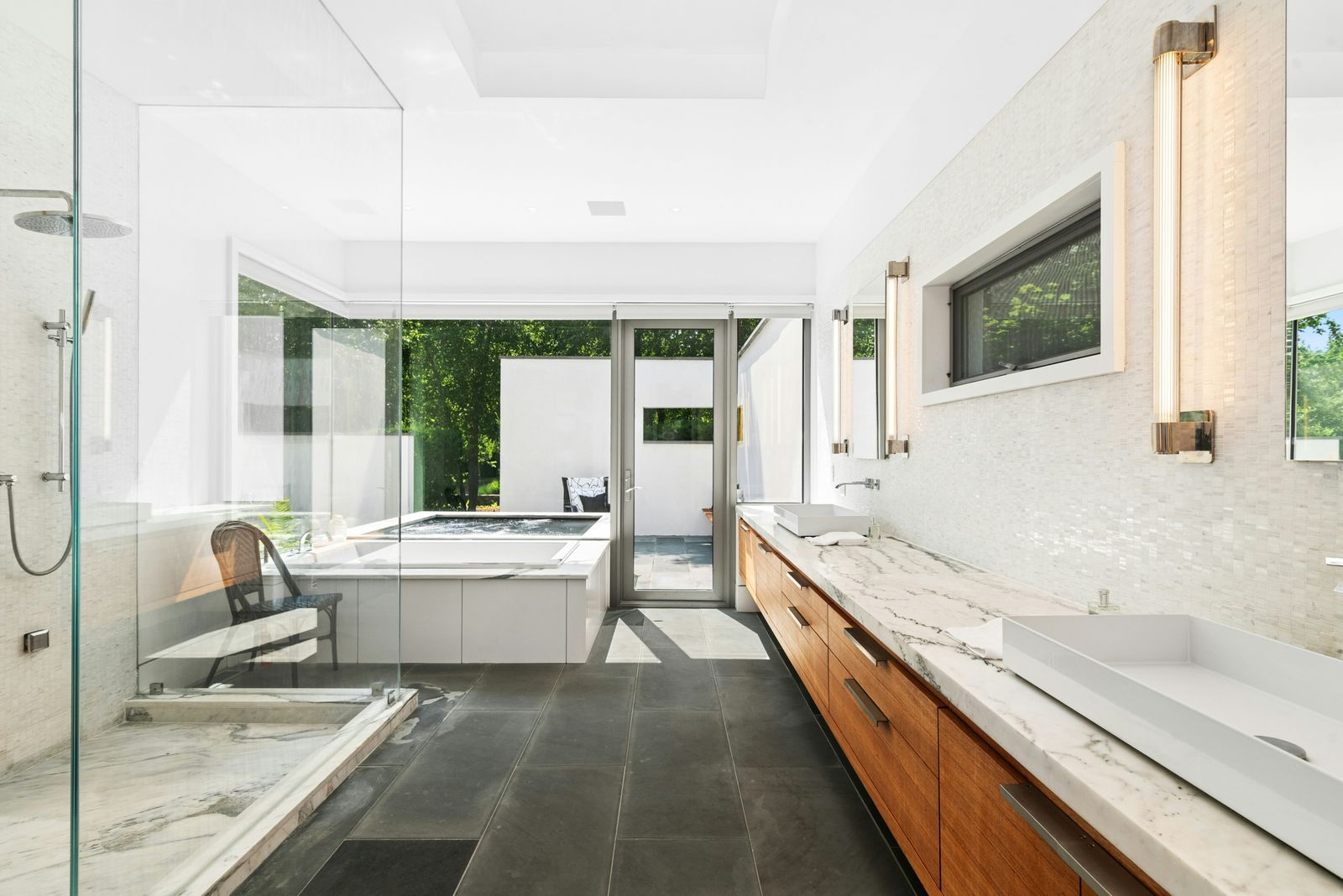 The suite's bathroom opens to darker stone flooring, with a long wood vanity running along one wall beneath a marble counter and twin vessel sinks. 