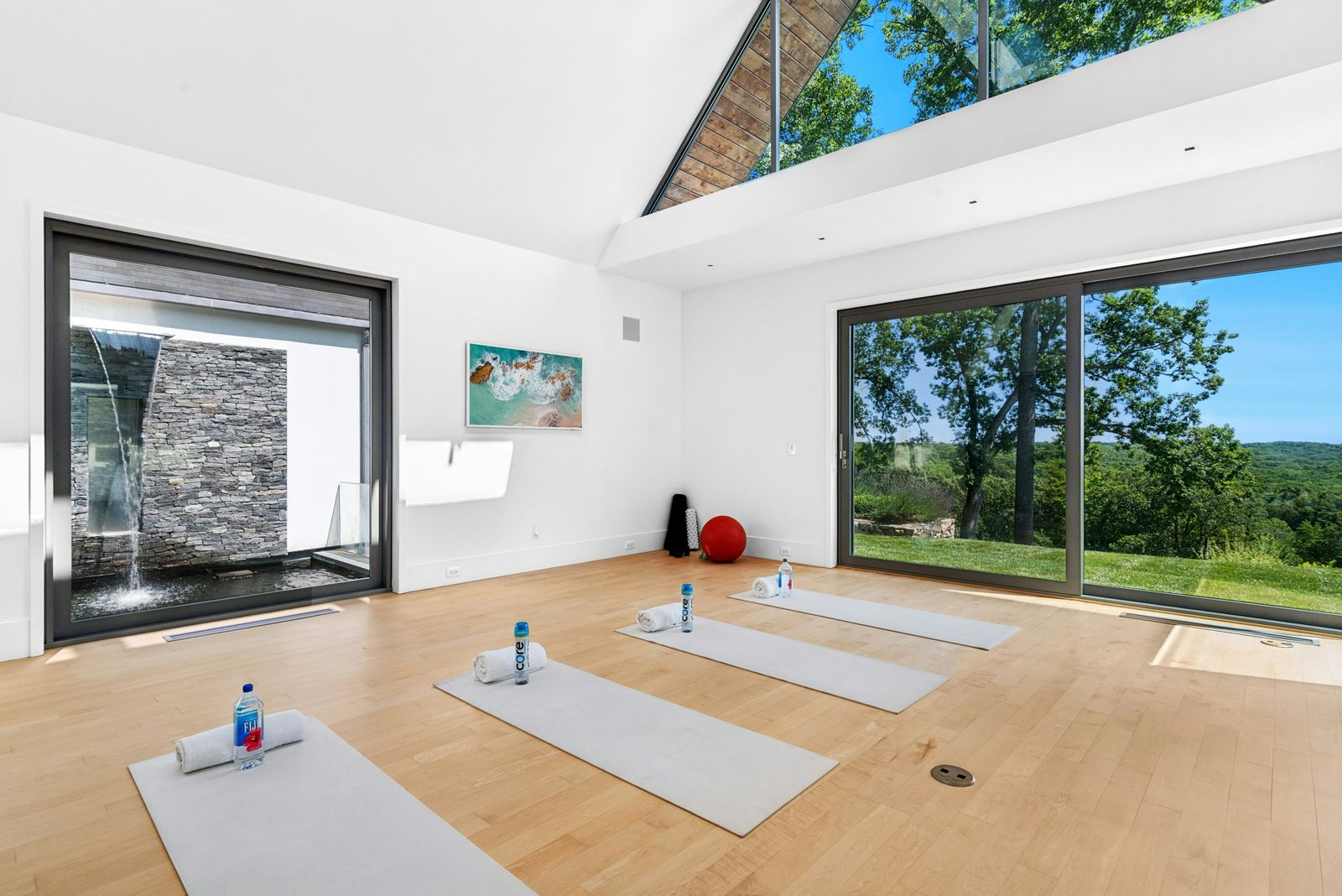 The private fitness room is set against a wall of sliding glass doors that opens the room to views across the lawn, while a large window looks directly toward one of the property’s cascading waterfalls.