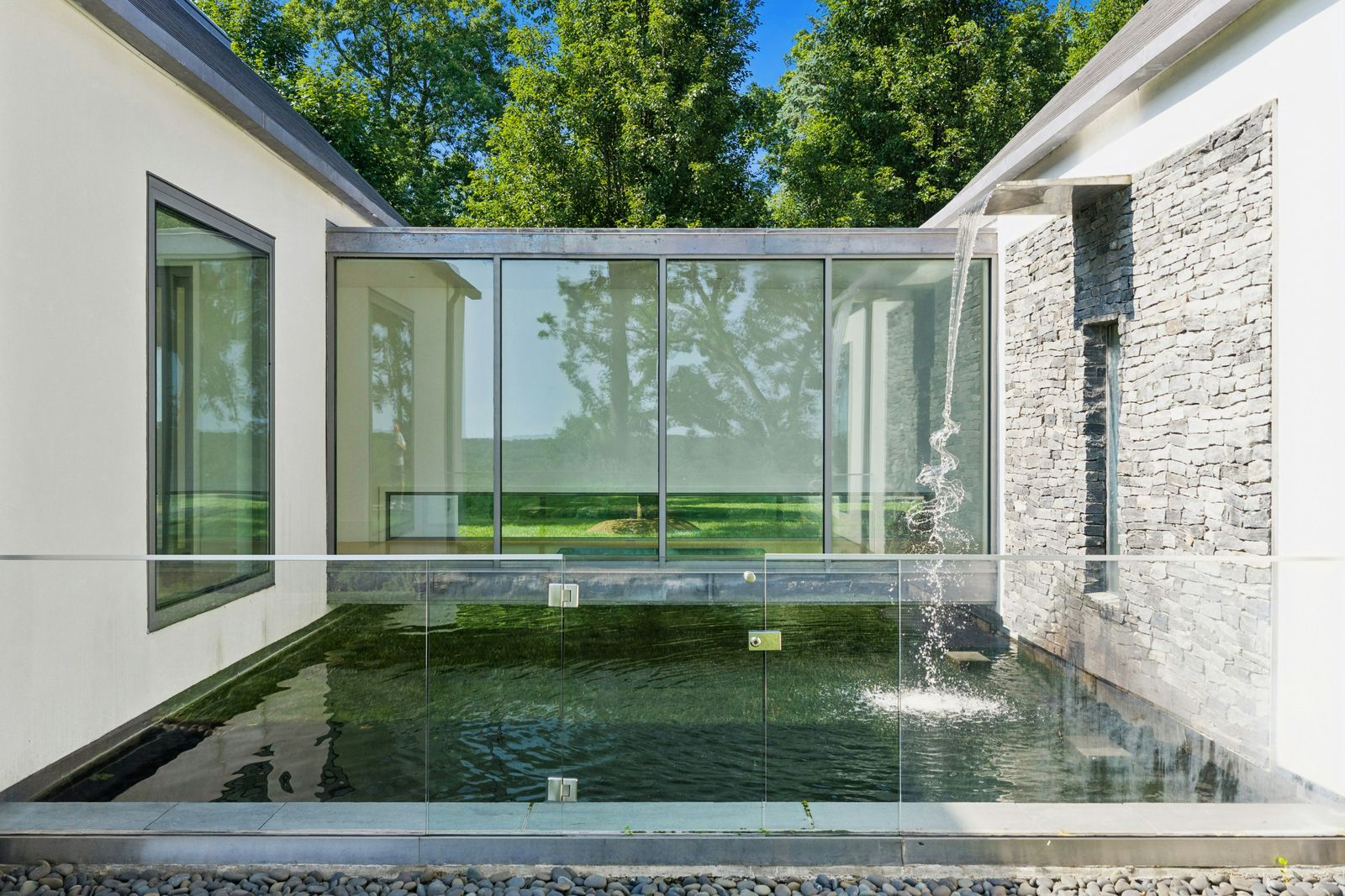 Two cascading waterfalls feed a series of dark reflecting ponds and narrow swimming channels, with koi moving between sections alongside planted edges and stone-lined walls.