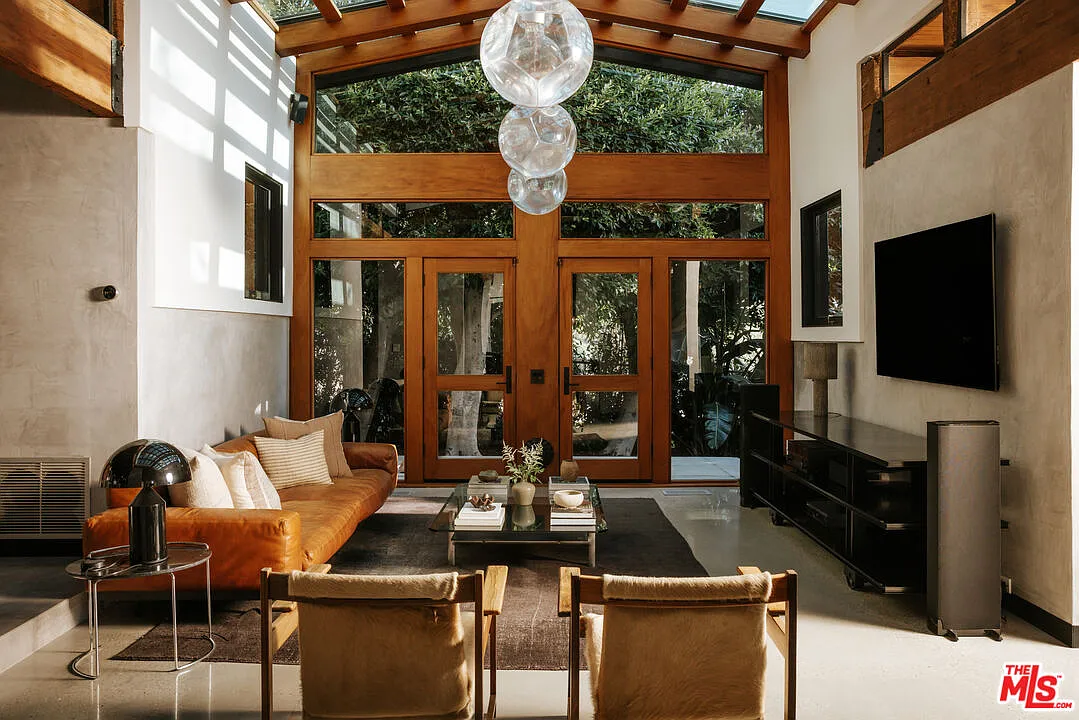 The space rises beneath a soaring timber-and-glass ceiling, with exposed wood beams continuing down the walls and large panes of glass framing surrounding greenery.