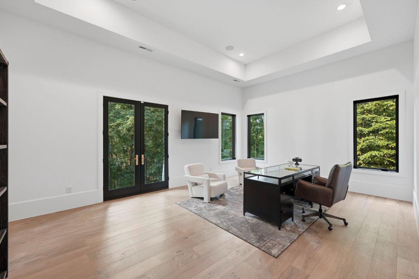 The office continues the minimalist black-and-white palette found throughout the house, with a glass-topped desk that sits beneath the tray ceiling and French doors opening to a small balcony.