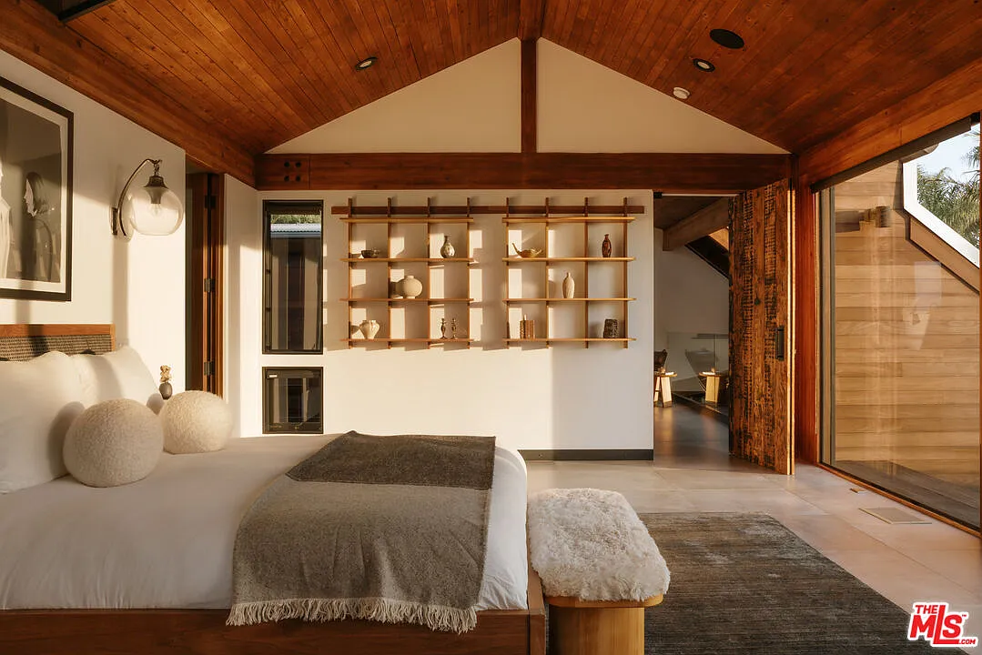 Built-in shelving and warm timber details extend the design palette from downstairs, while a full wall of glass doors opens directly onto a private terrace facing the ocean.
