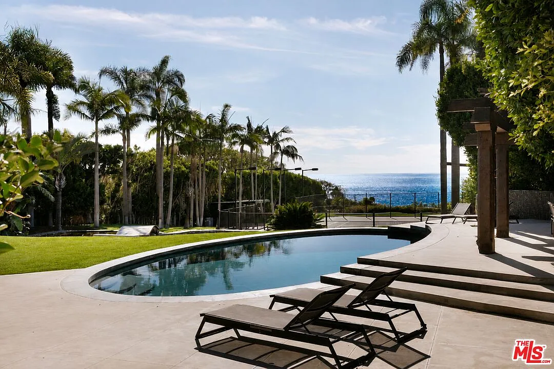 A curved swimming pool is surrounded by a broad stone patio.