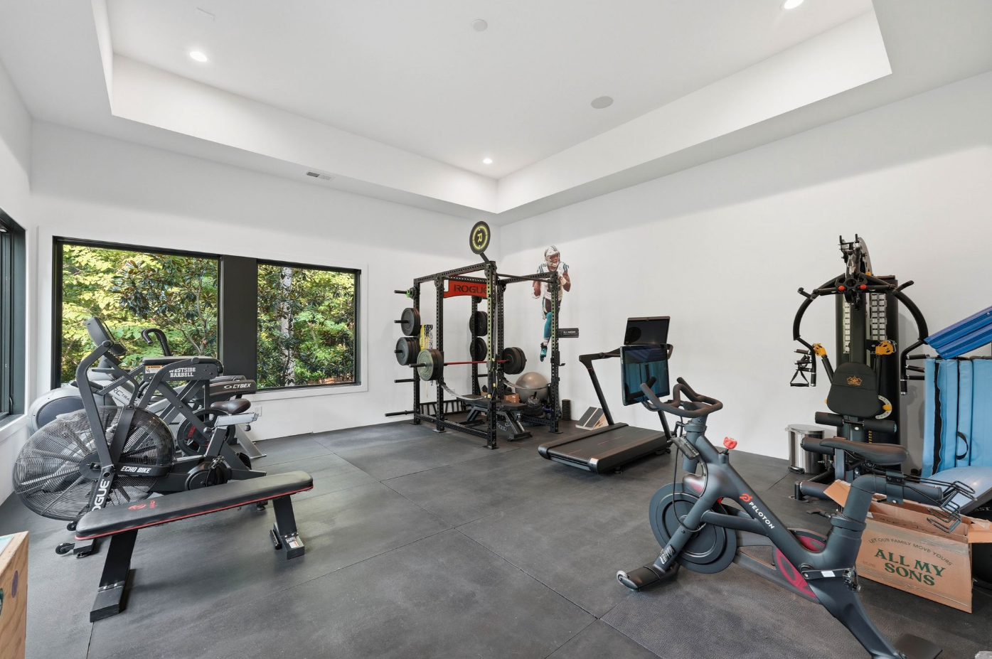 The room accommodates cardio equipment, free weights, a squat rack, and a multi-workout strength machine while keeping enough open floor space for stretching and floor exercises.