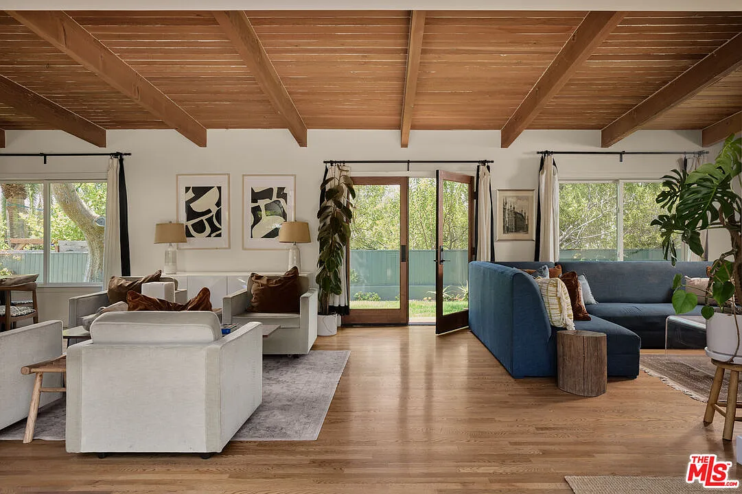 Main living spaces beneath a vaulted, wood-beamed ceiling, with double glass doors at the center opening directly to the side yard.