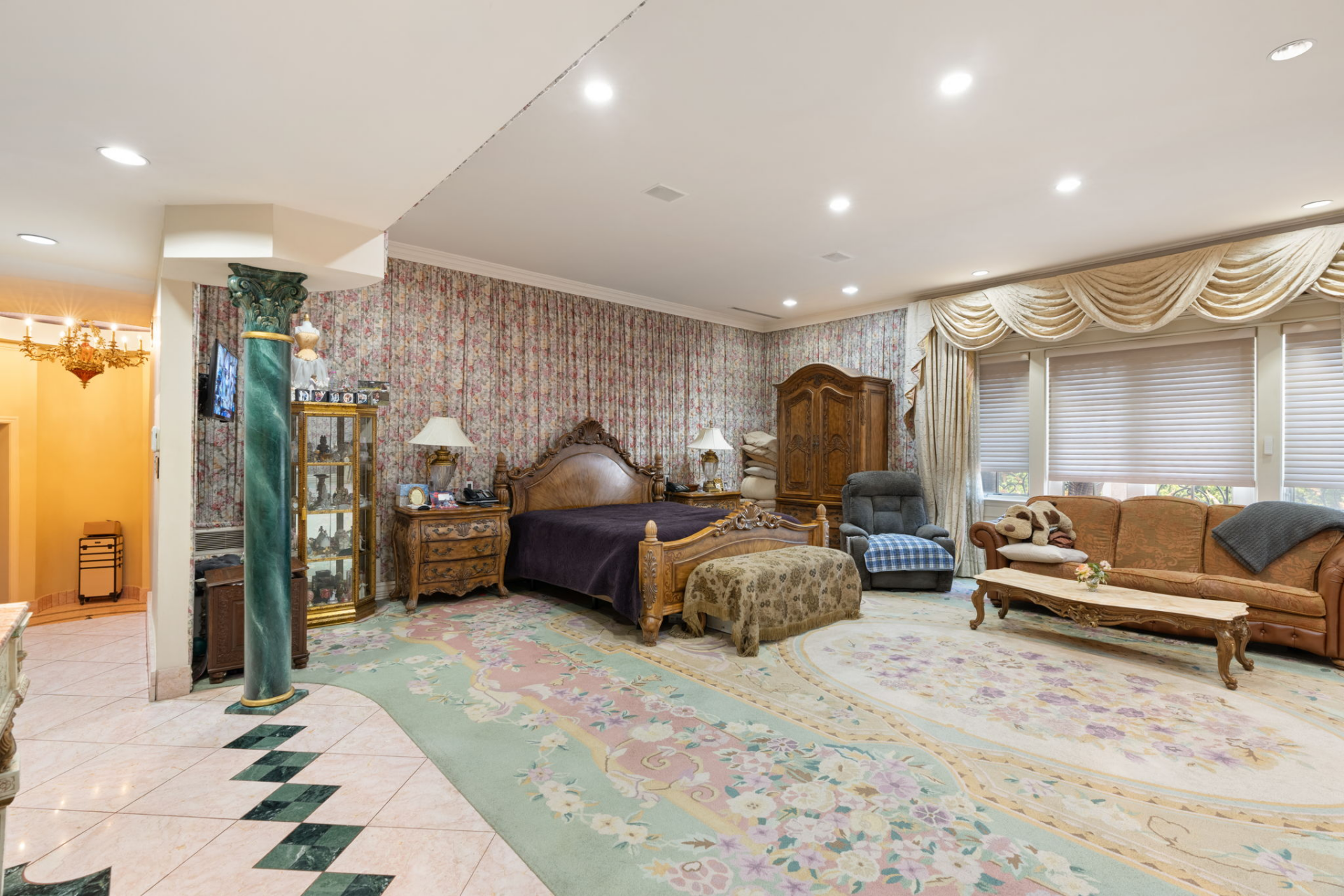 The primary bedroom is generously sized, with a carved wood bed, floral wallcovering, and a large patterned carpet.