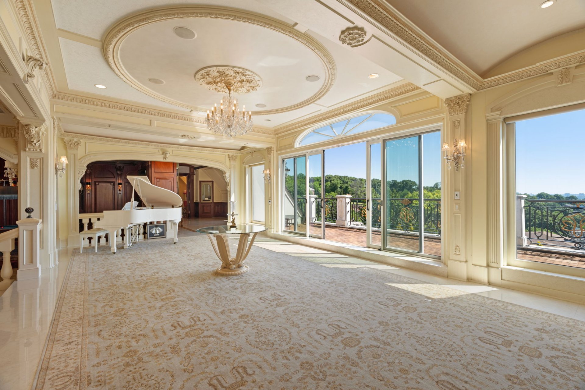 A white grand piano sits in the corner, while oversized glass doors and windows line the opposite wall, opening to a rooftop terrace.