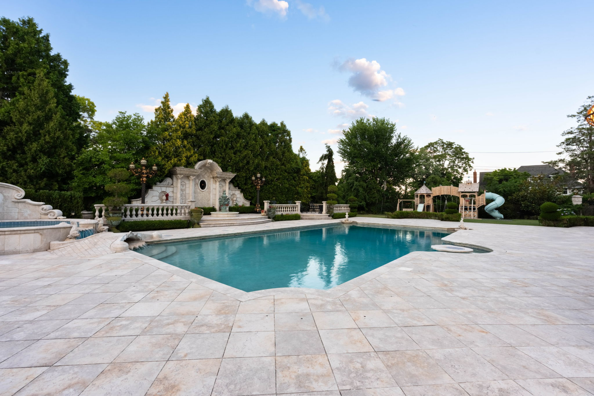 Decorative fountains, balustrades, sculpted landscaping, a playground, and multiple levels of terraces continue around the water, giving the entire pool area the scale of a private resort.