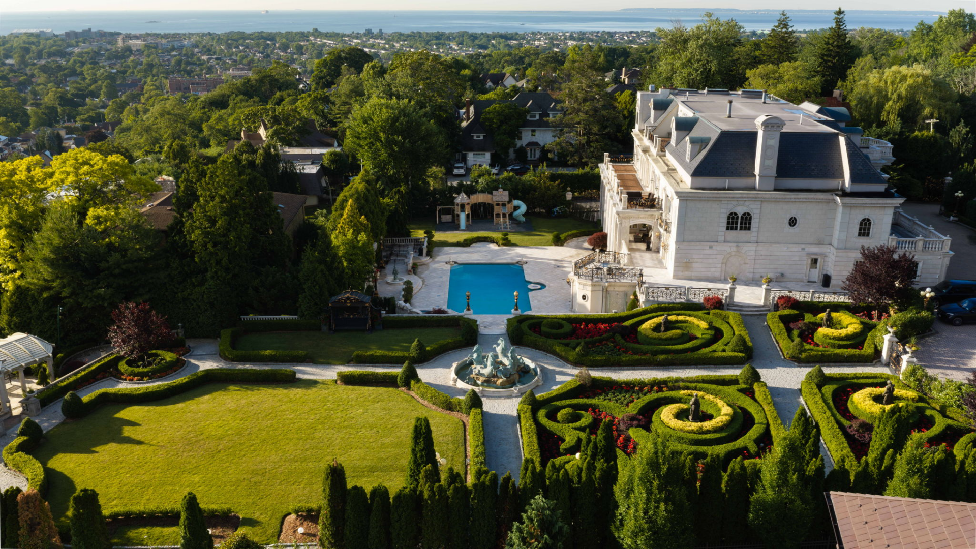 Beyond the pool, the grounds open into carefully maintained botanical gardens laid out with clipped hedges, shaped topiary, flower beds, fountains, and stone pathways.