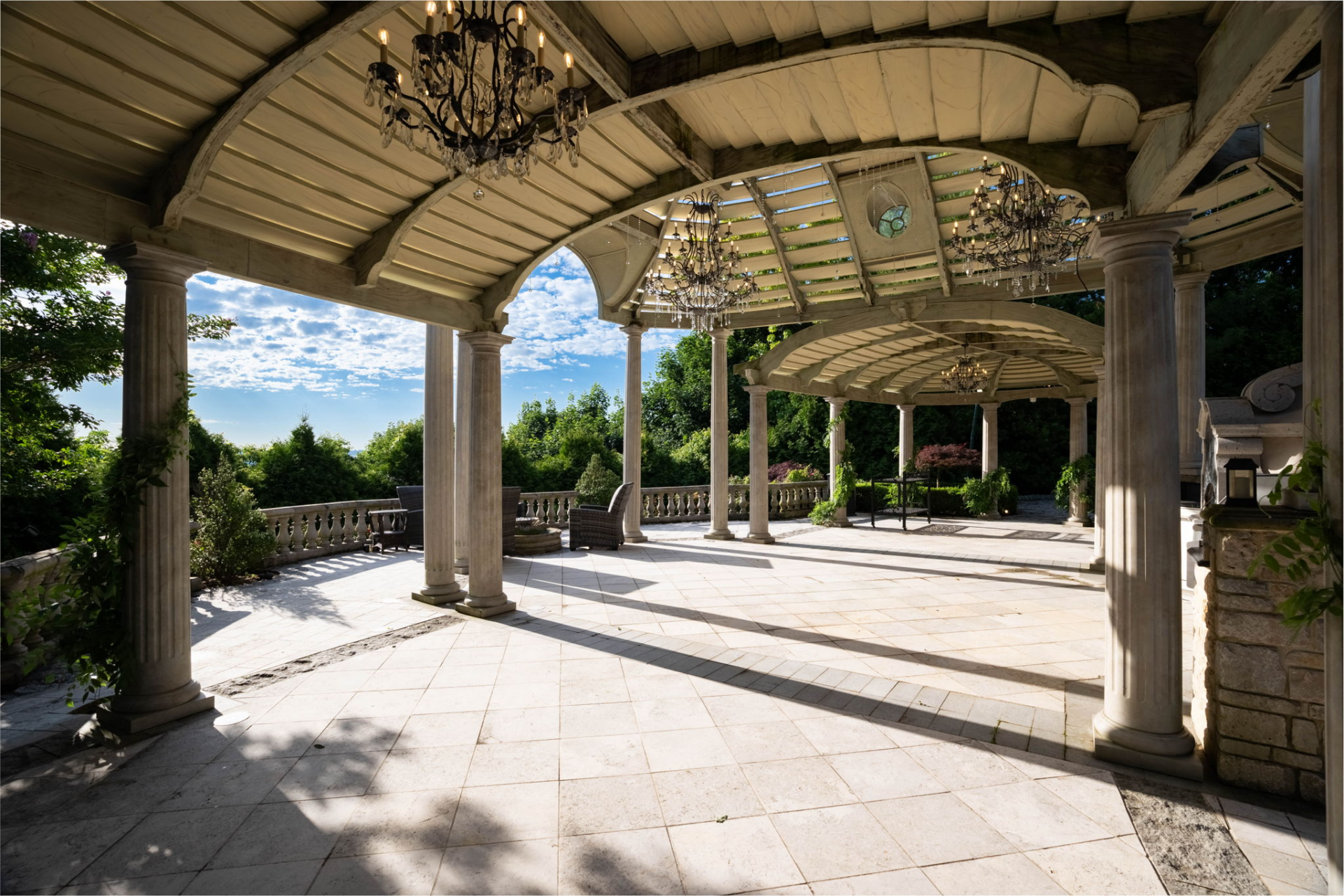 A large covered gazebo is supported by columns and finished with chandeliers overhead, creating a sheltered entertaining space with harbor views.