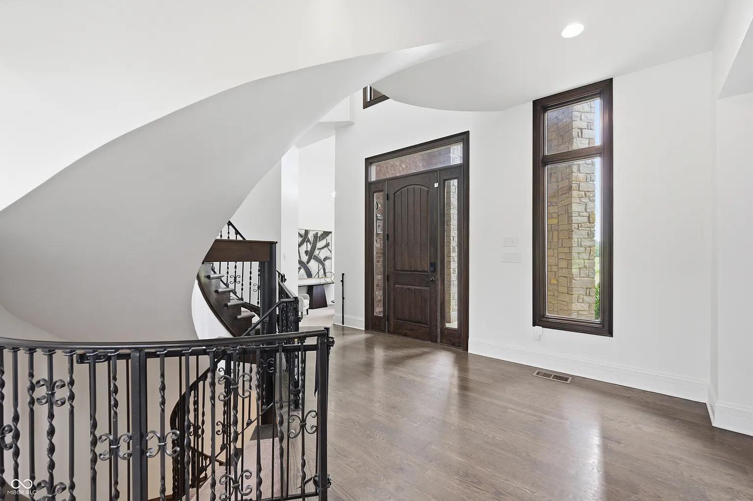 The entry immediately opens around a split-level spiral staircase, with dark wood floors and wrought-iron railings.