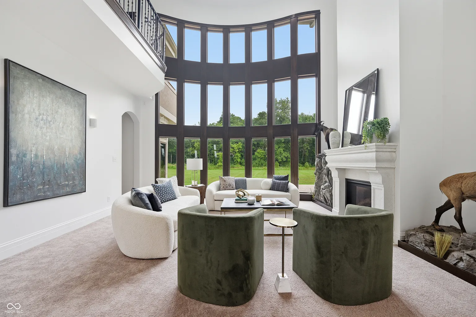 A fireplace sits across from curved sofas and a pair of green lounge chairs beneath the open second-floor gallery.
