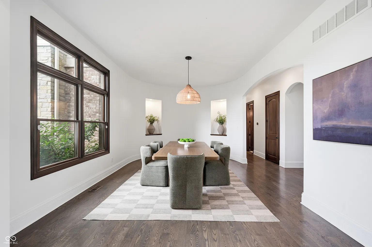 The formal dining room features a long wood dining table beneath a woven pendant light, while tall black-framed windows along one wall bring in natural light.