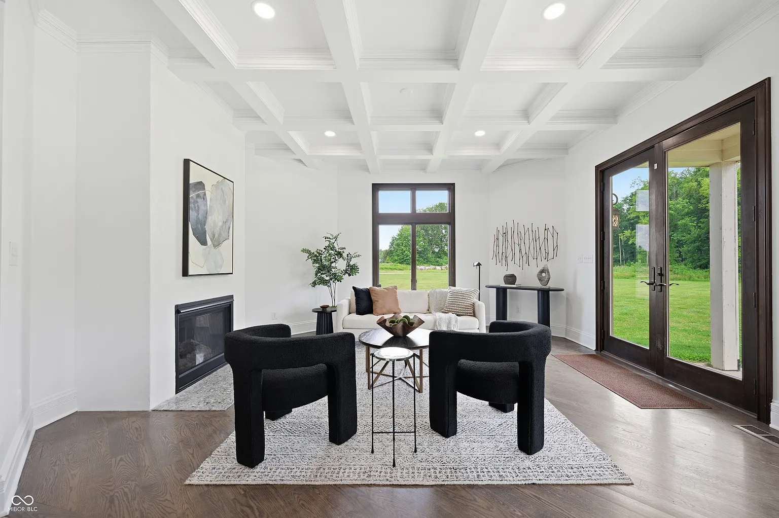 The seating area is arranged around a compact fireplace set into the side wall, while a mix of curved black chairs and a light sofa offer a place to sit before glass doors open to the covered patio.