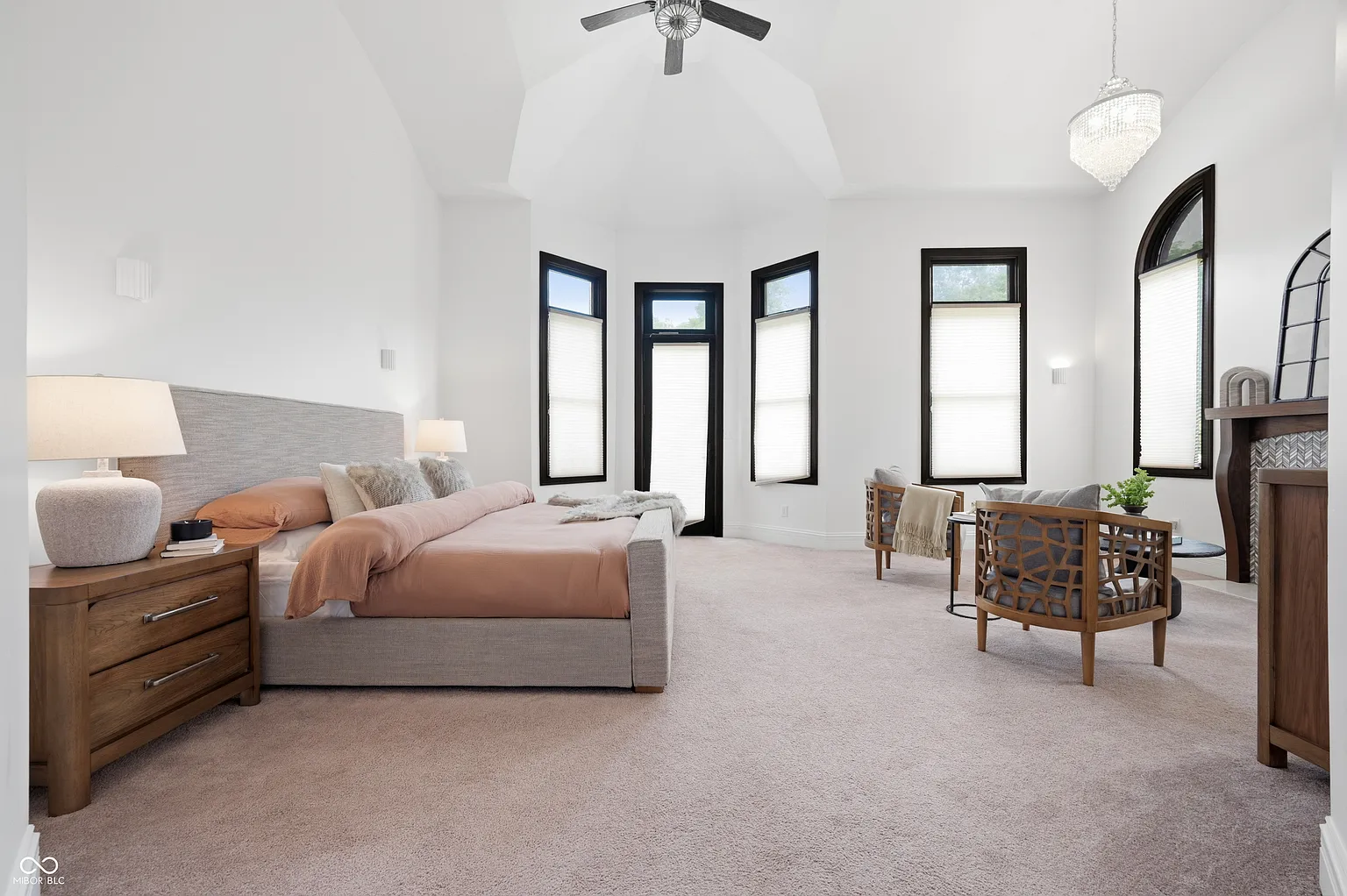 Also on the main level is the primary suite, which opens beneath a tall vaulted ceiling with dark-trimmed windows lining the exterior walls.