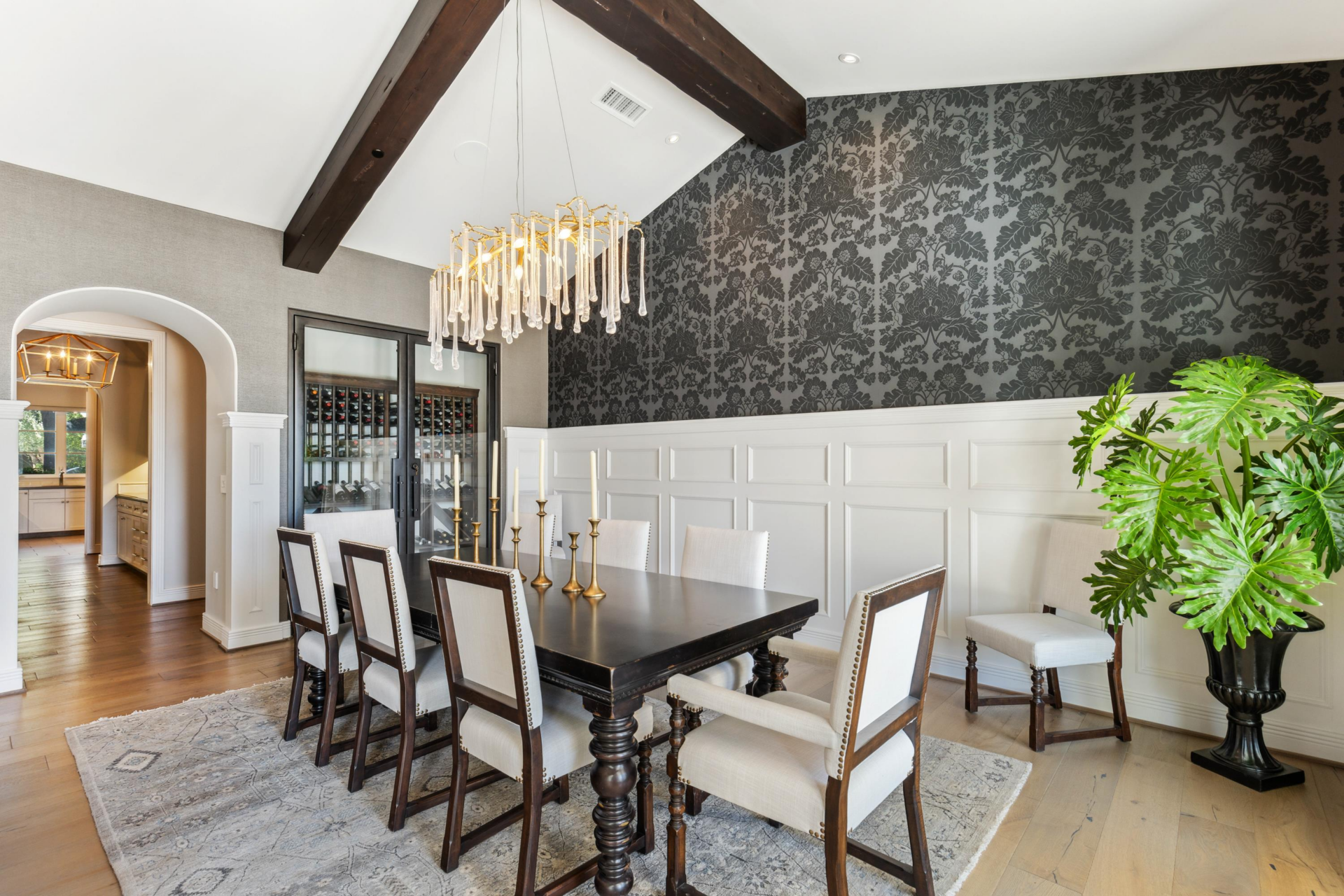 The formal dining room, where hardwood floors and paneled lower walls continue beneath a designer chandelier and dining table set for eight. 