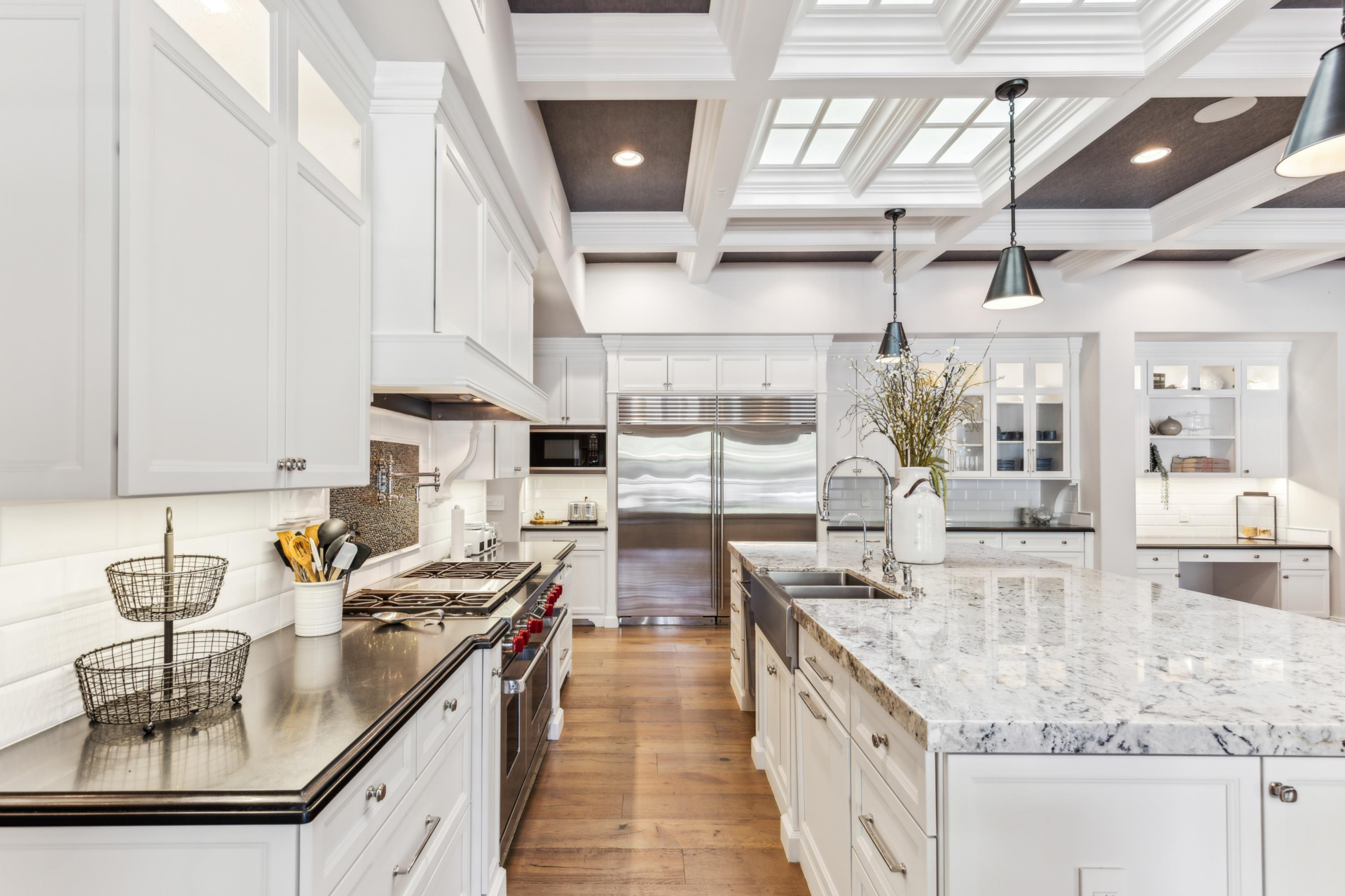 White cabinetry wraps the walls around a professional-style range, oversized stainless-steel refrigerator, and additional built-in appliances.