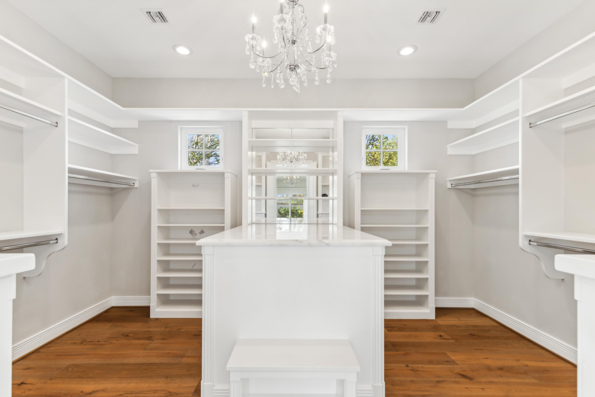 A large walk-in closet lined with custom white shelving, drawers, and hanging rods. 