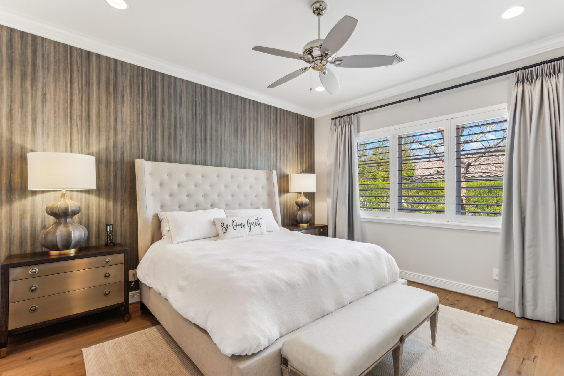 The guest bedroom features a tall upholstered headboard and a vertically textured accent wall running behind the bed. 