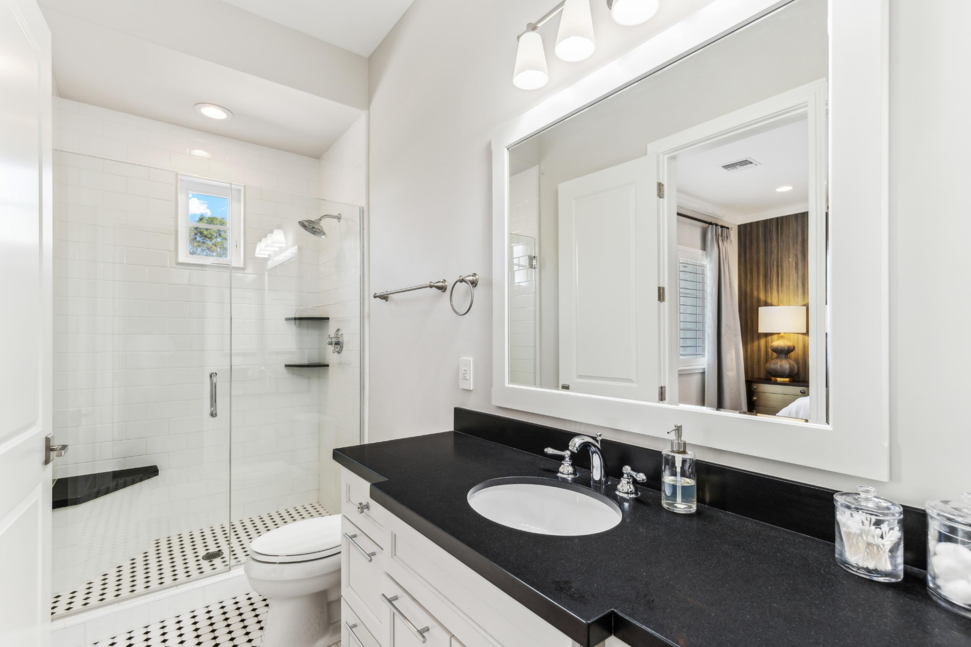 Its en-suite bathroom continues the black-and-white palette with a long black stone vanity, white cabinetry, and a glass-enclosed shower lined in white subway tile. 