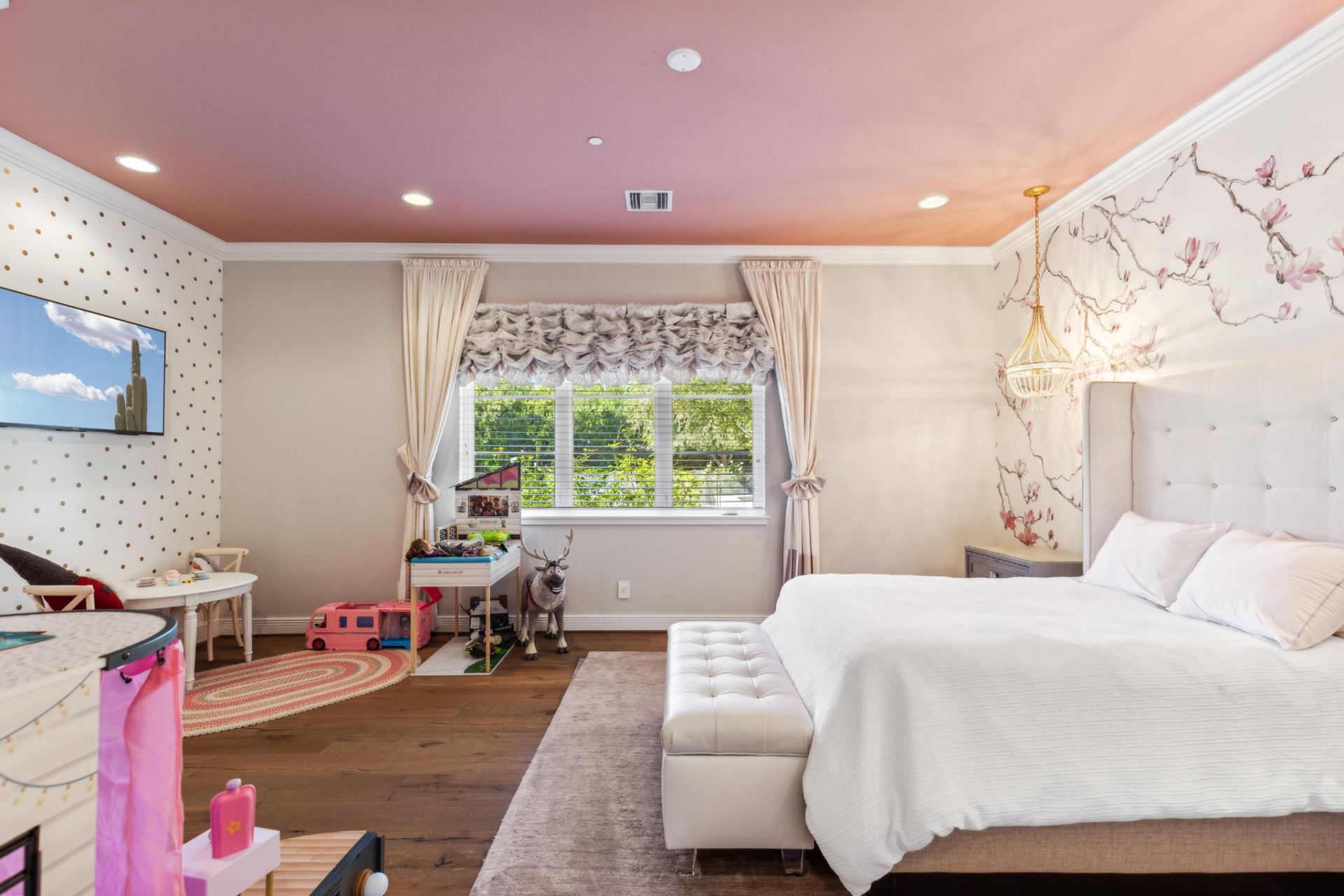 The girls’ bedroom shifts into a softer palette, with a dusty pink ceiling, floral wallpaper behind the bed, and gold pendant lights dropping over the bedside tables. 