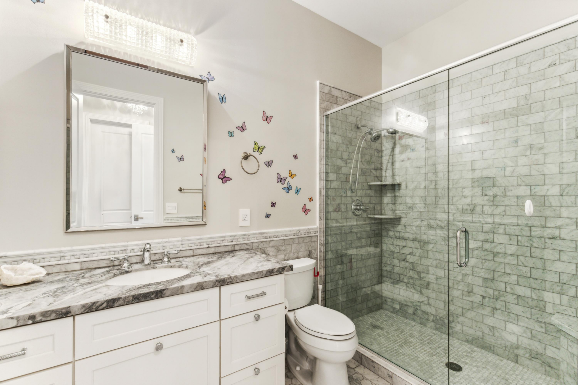 The connected bathroom picks up the more delicate detailing with butterfly decals climbing the wall beside marble counters and the glass-enclosed shower.