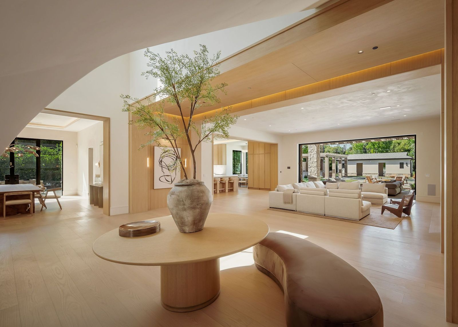 Set beneath the sweep of the staircase, the area is furnished with a round wood table and curved bench, creating a natural place to pause before moving into the surrounding rooms.