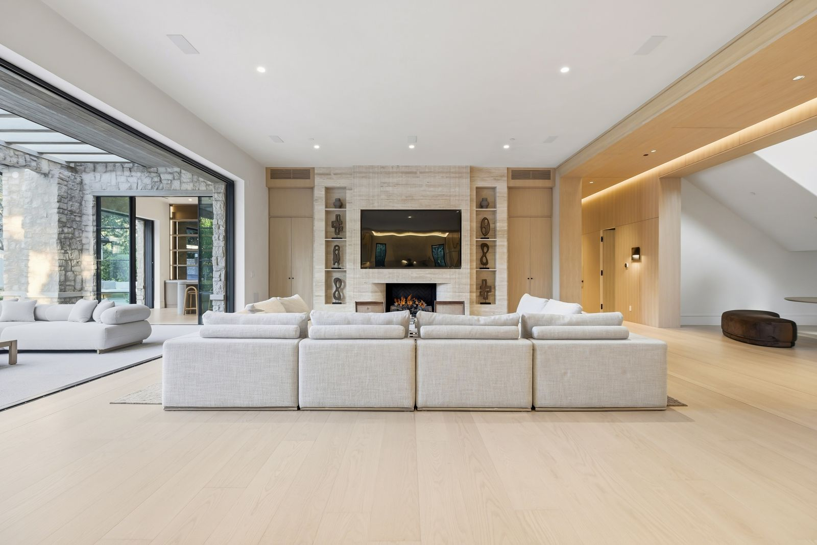 The central gathering space opens into an oversized great room where a long sectional faces a fireplace and TV set into a textured stone wall. 