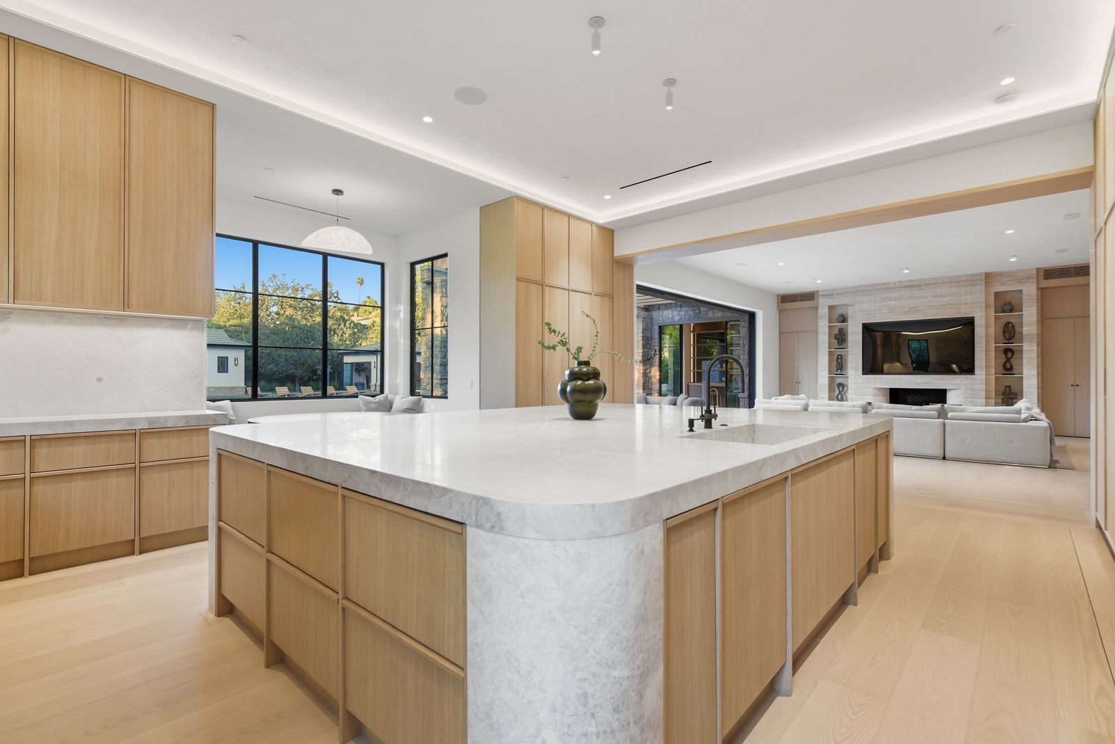 A few steps from the great room, the kitchen centers on an oversized island wrapped in Taj Mahal natural stone, with softly rounded corners and deep white oak cabinetry built underneath. 