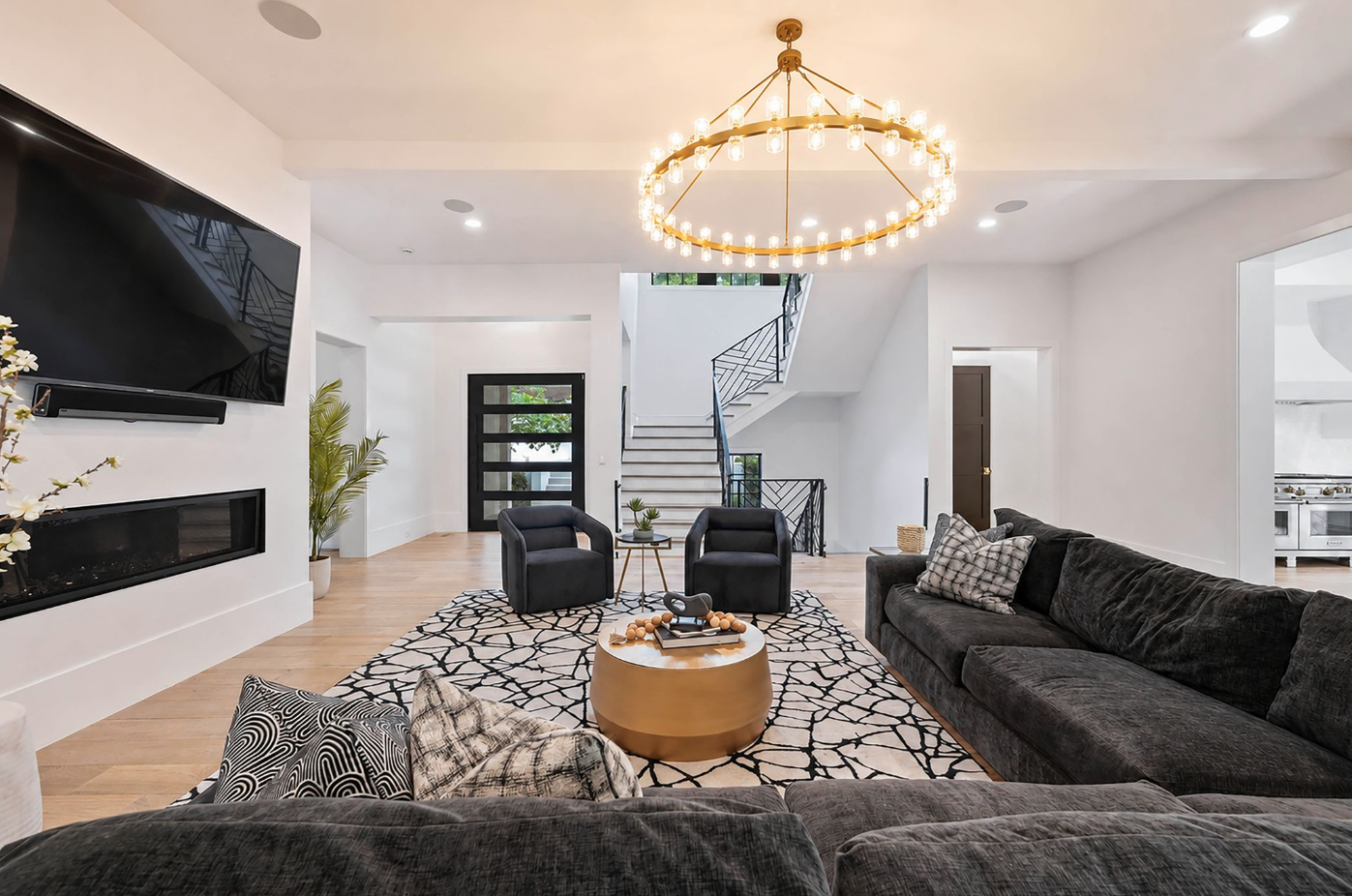 A pair of charcoal sectionals and curved lounge chairs form the main seating area beneath a large circular brass chandelier.