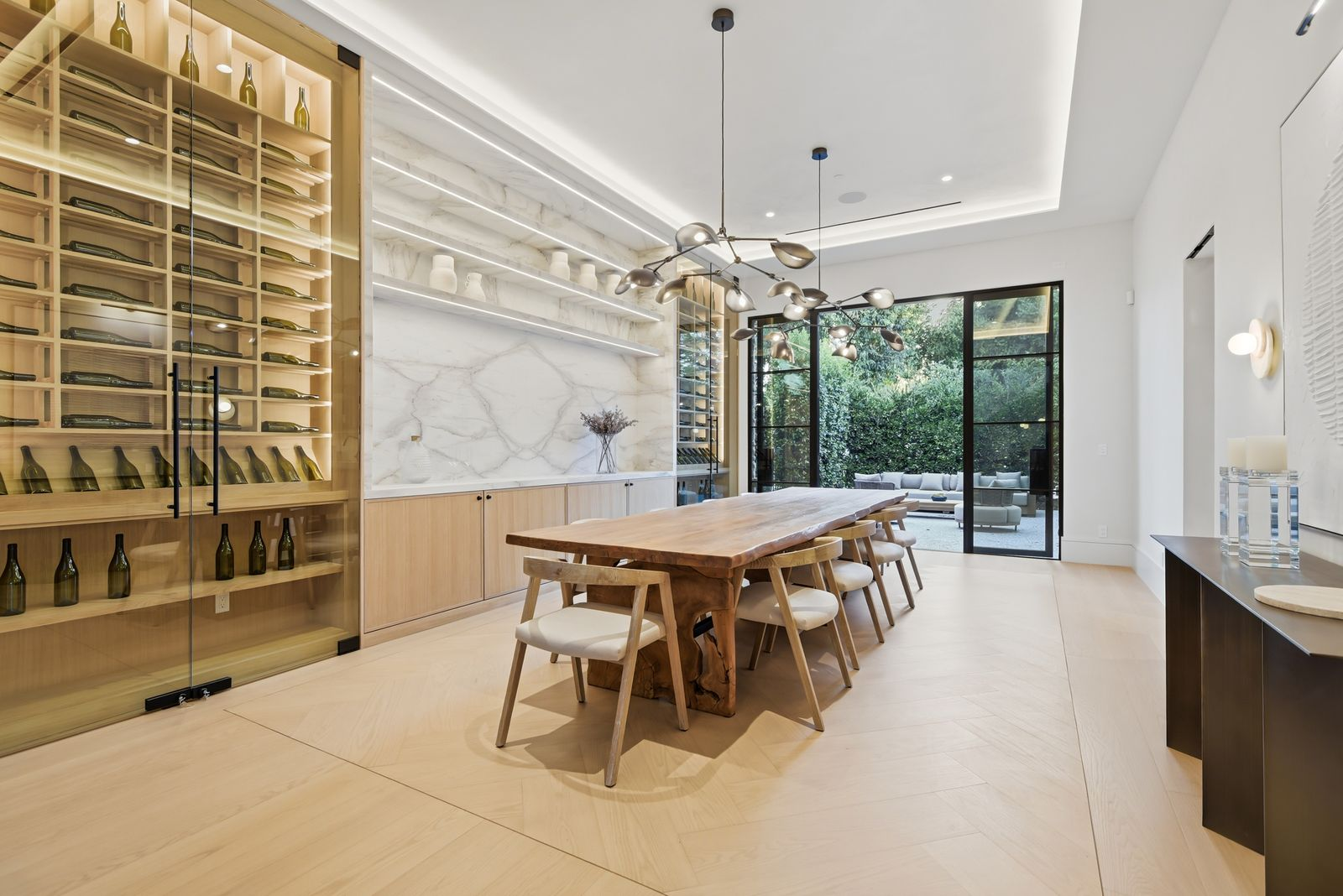 Dining room where a long wood table sits between two floor-to-ceiling glass wine displays built into the walls.