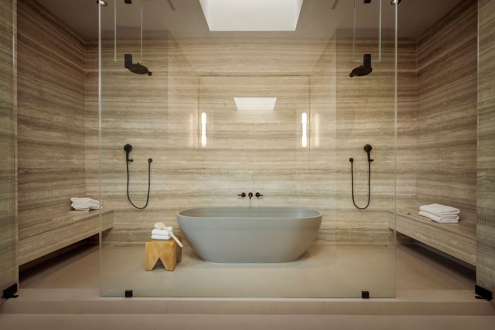 A deep freestanding soaking tub framed by two shower stations within a glass-enclosed wet room. 