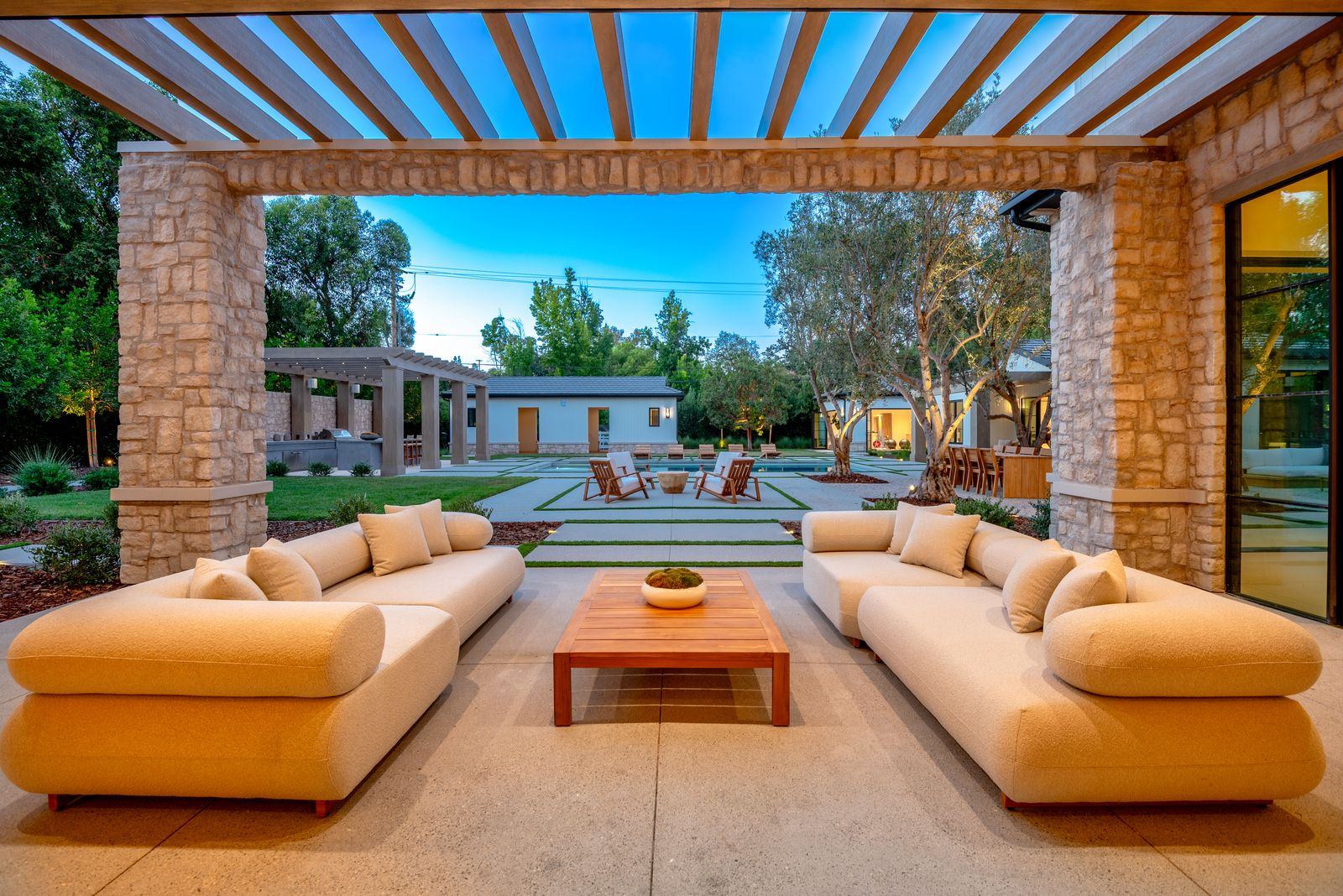 Two oversized sofas face each other around a low table, looking out across the entire backyard toward the detached guest house, separate gym, and barn.