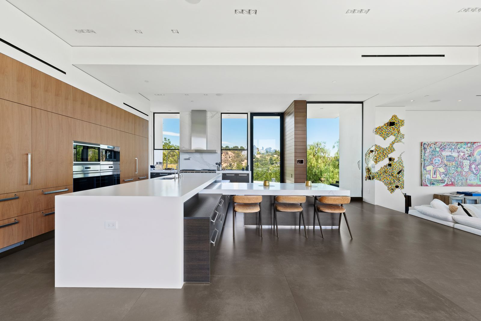 The larger island is wrapped in crisp white and provides an expansive prep surface, while the connected breakfast counter extends toward the den with seating for four.