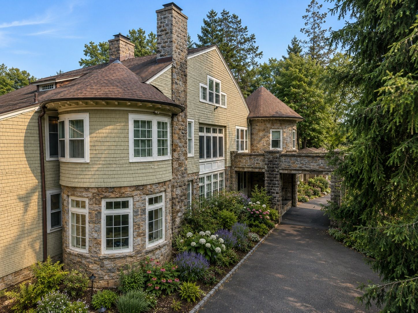 The exterior combines shingle siding, rounded stone bays, and tall chimneys, all enclosed by towering trees.