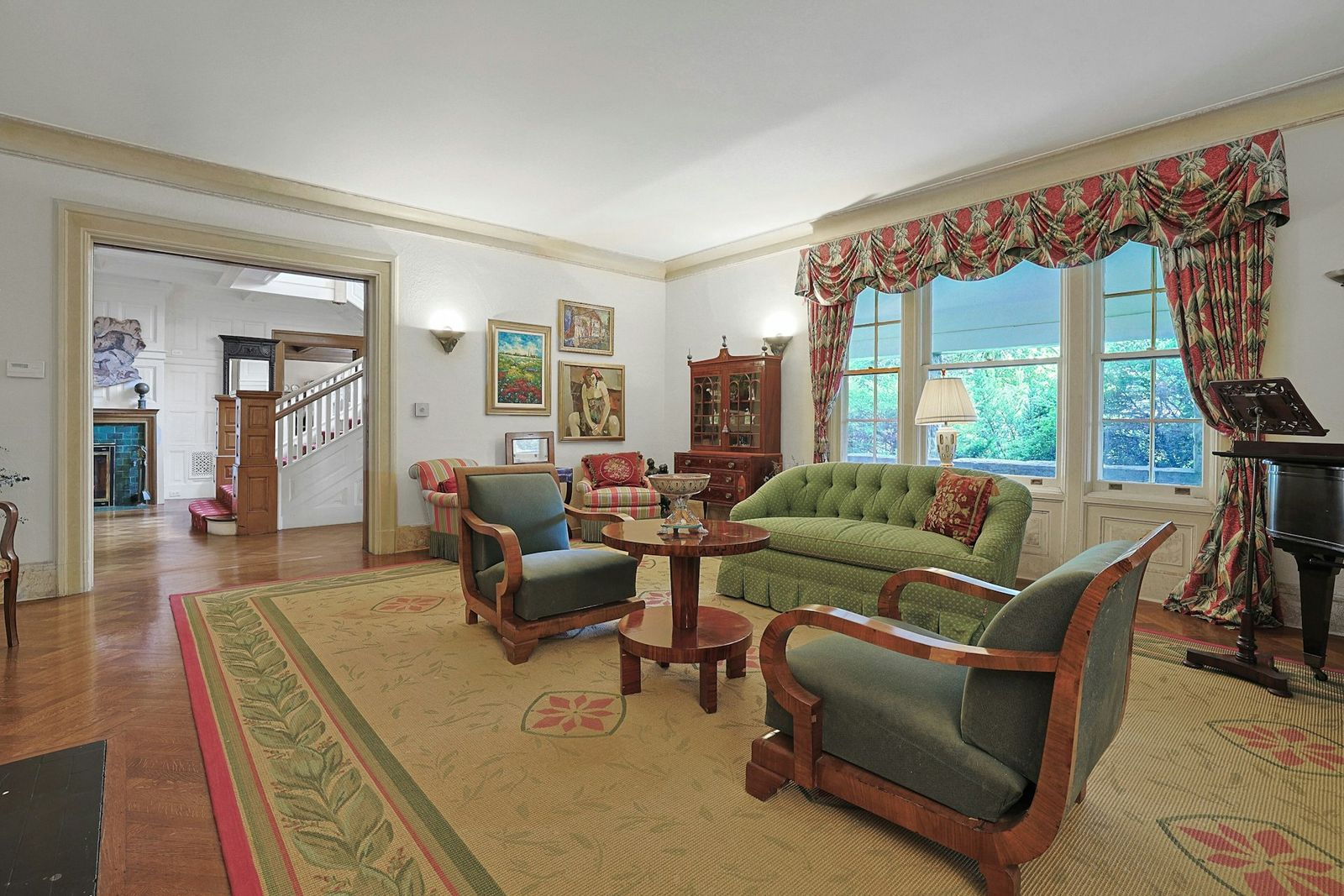 Facing the fireplace, a green tufted sofa is paired with two wood-framed armchairs upholstered in a darker green fabric, while additional striped armchairs fill out the far side of the room.