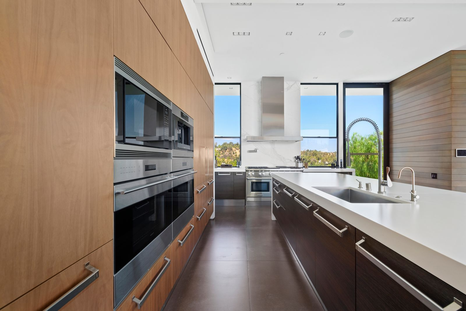 Warm wood cabinetry conceals much of the storage and refrigeration, while darker lower cabinets add contrast beneath the counters. 
