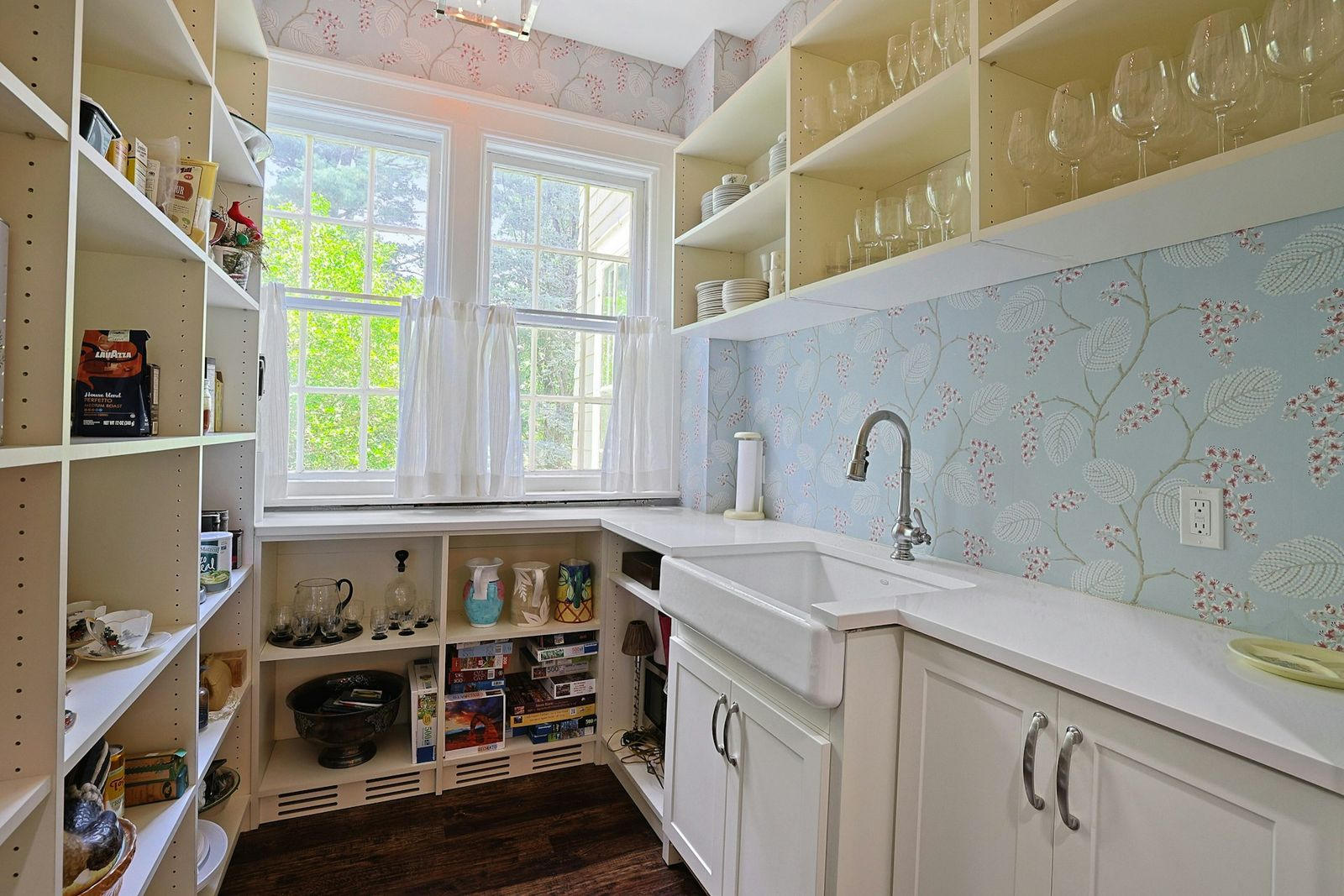 Just around the corner, the kitchen extends into a separate butler’s pantry, where open shelving filled with food and glassware climbs both walls around a long counter with a farmhouse sink.