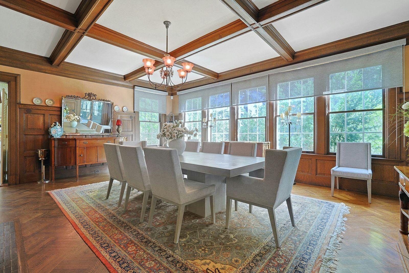The formal dining room, where a large table for eight is set beneath a decorative chandelier and a coffered ceiling trimmed in dark wood. 