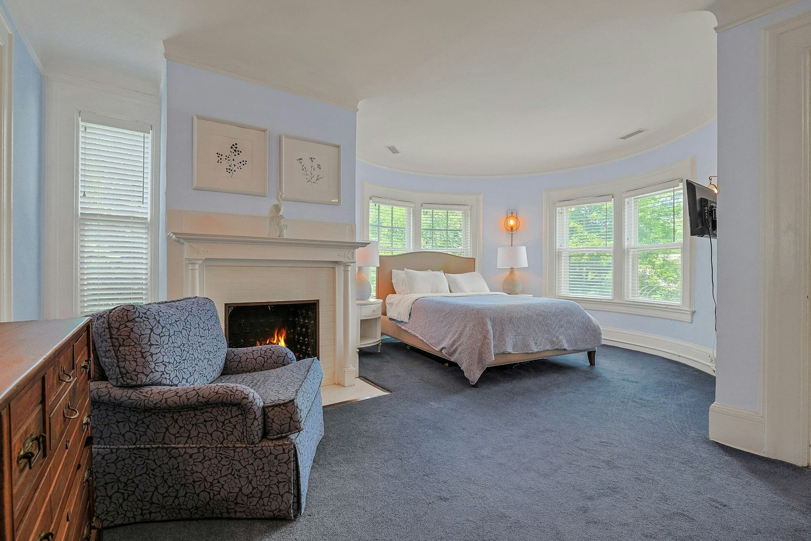 Another bedroom sits in one of the home’s rounded bays, where pale blue walls and a curved bank of windows shape the sleeping area. 