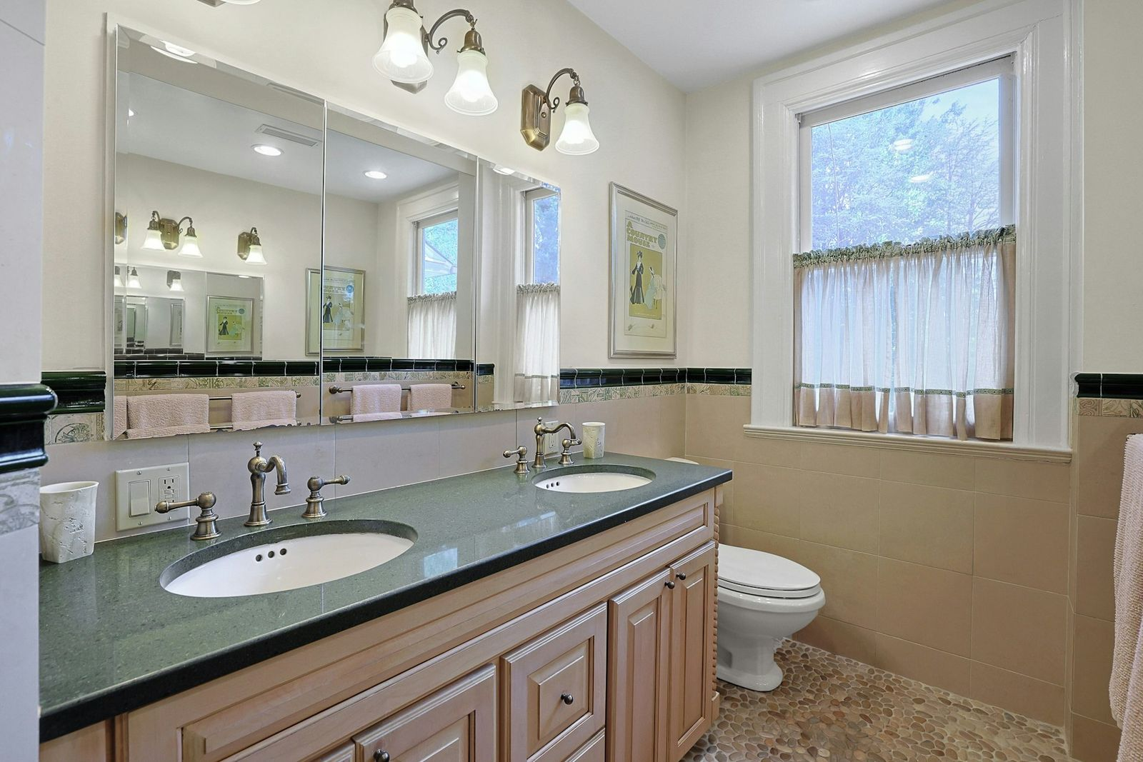 The suite's bathroom features a long double vanity topped in dark stone, framed by large mirrored panels and traditional brass-toned fixtures. 