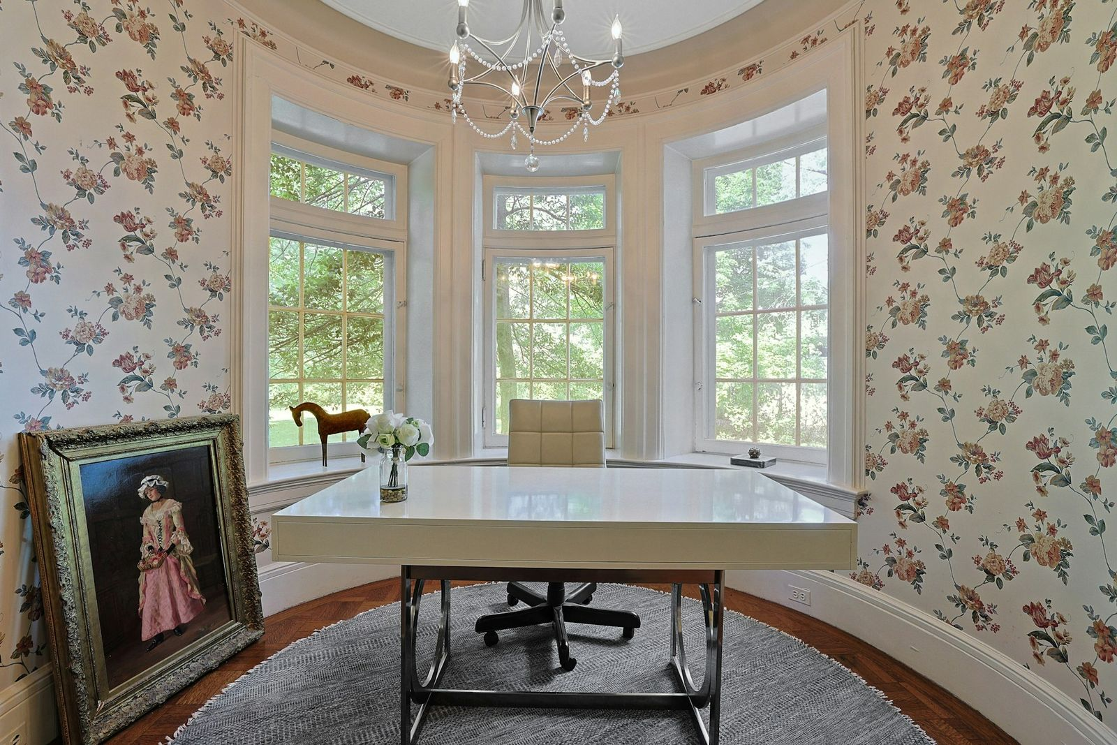 A shiny white desk sits directly in front of the windows beneath a delicate chandelier, giving the room a lighter, more feminine look.