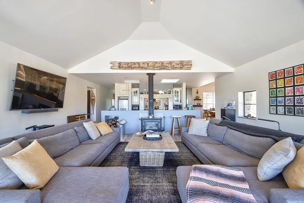 Two oversized sofas face each other across a wood coffee table, while a freestanding wood-burning stove sits along the far wall between the lounge and the kitchen.