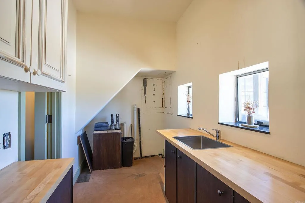 Just off the bedroom is a private laundry room with butcher-block counters, a utility sink, dark lower cabinetry, and additional storage built into the walls. 