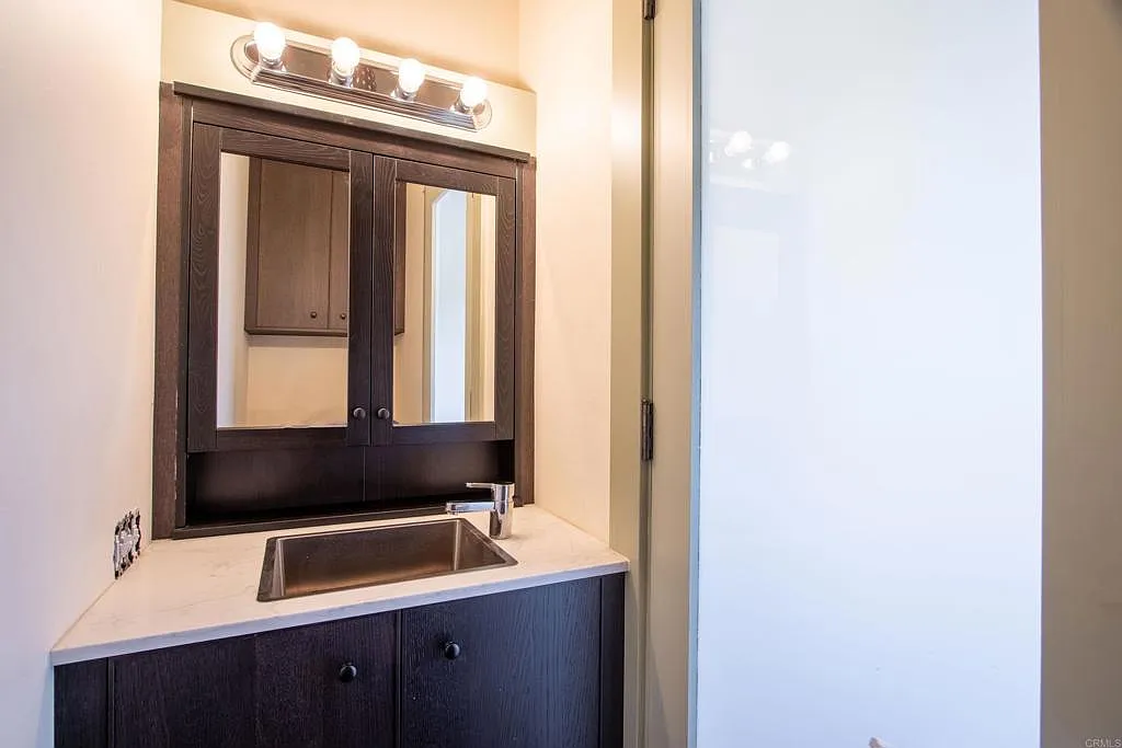 The suite also includes its own half bath, finished with a compact vanity, dark cabinetry, and a large mirrored medicine cabinet.