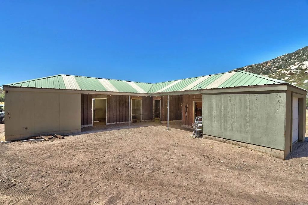 The equestrian setup begins with a long L-shaped horse barn arranged placed in a central dirt courtyard, with multiple stalls. 