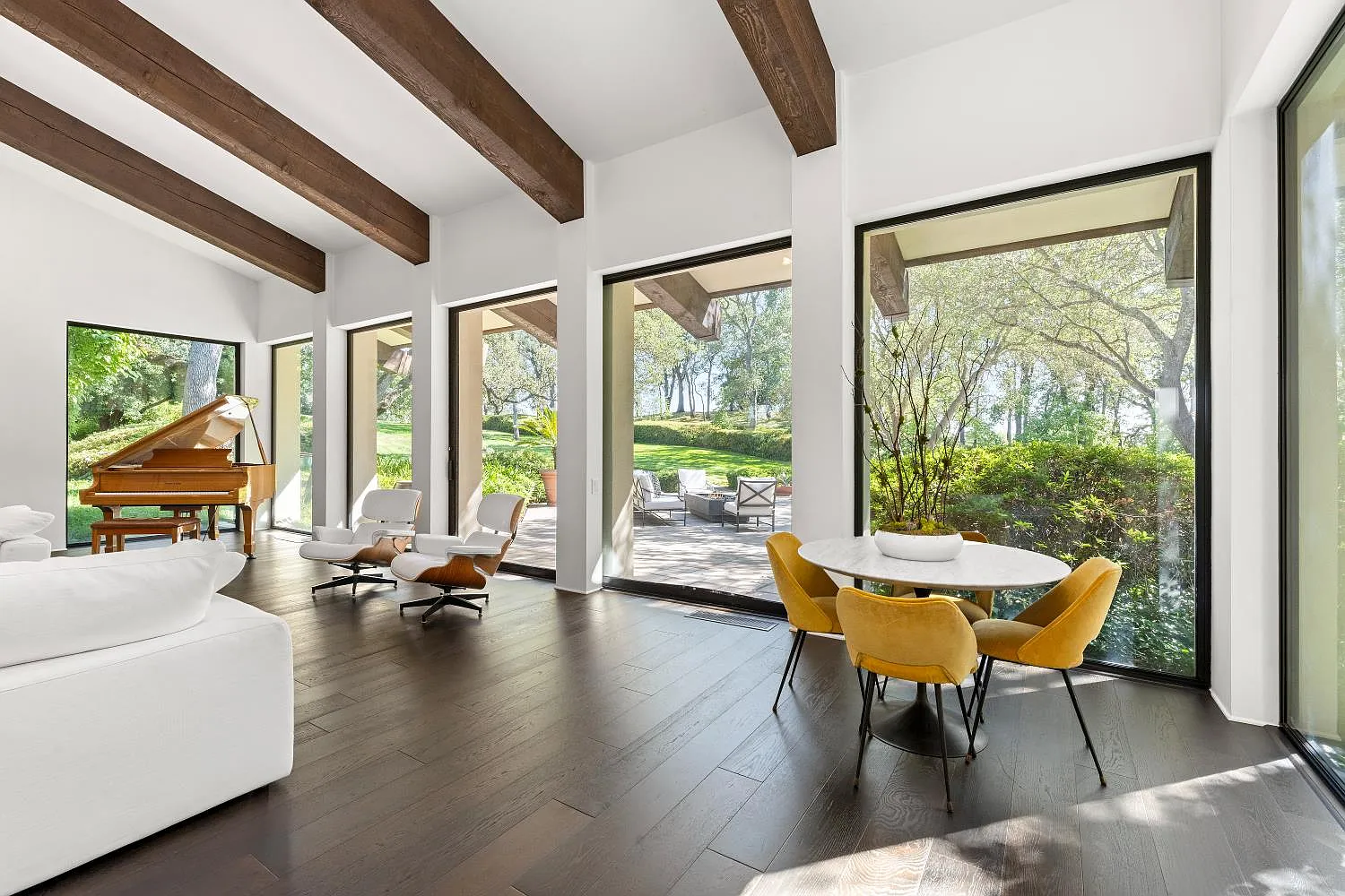 A piano and small dining area sit along the windowed side of the room, extending the space toward the outdoors while keeping the overall layout open.