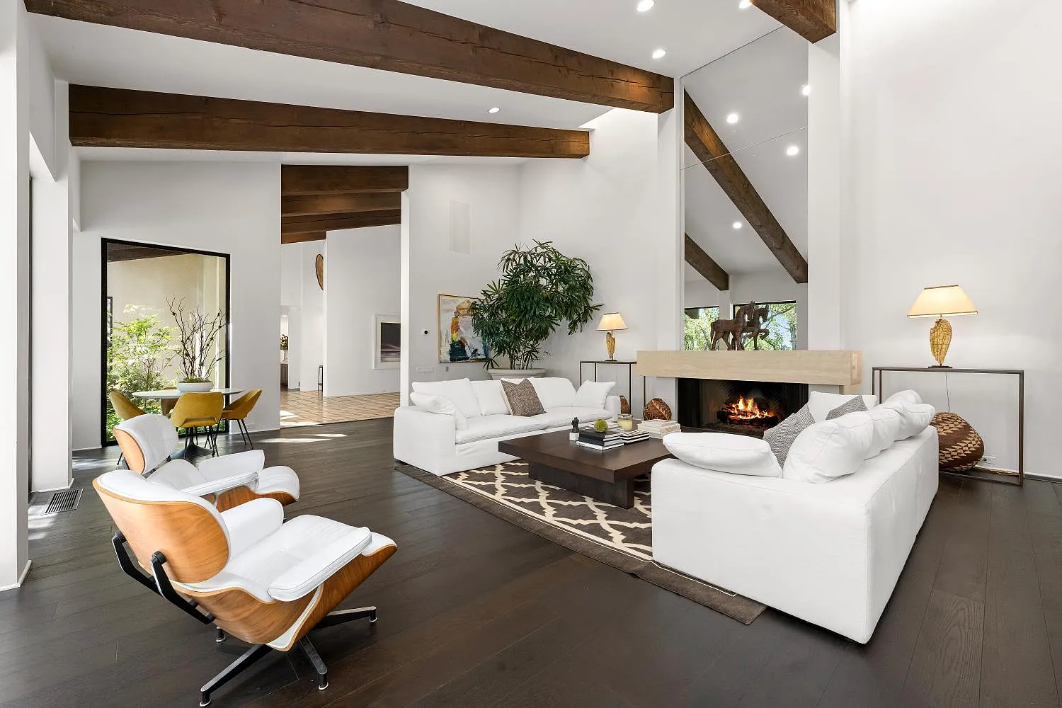 Formal living room where exposed wood beams stretch across the high ceiling above a pair of white sofas arranged around a low coffee table and fireplace.
