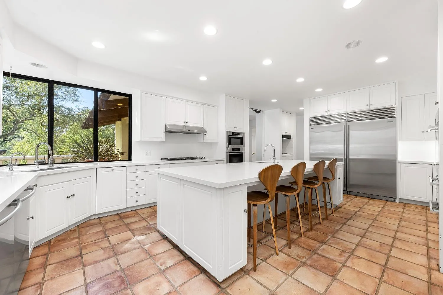 Terracotta tile flooring continues from the main hall, while a wide window above the sink brings warmth and natural light into the room.