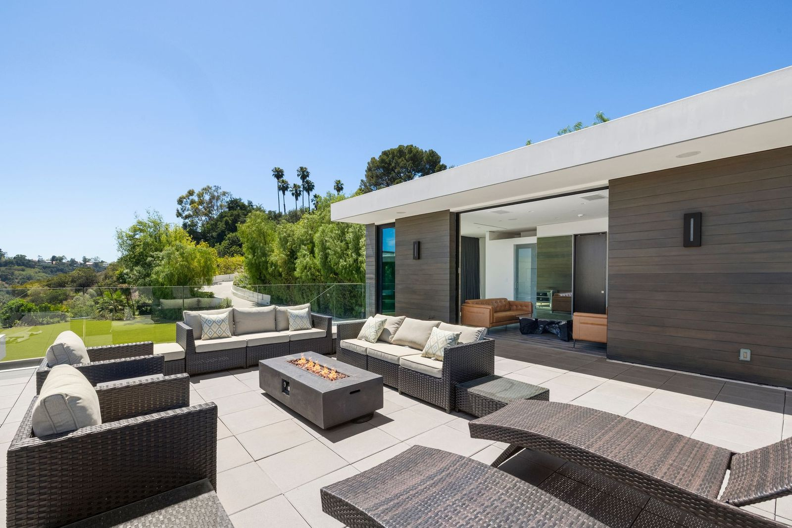 Outdoor sofas and loungers gather around a linear fire pit, creating a separate elevated living area with wide views across the property and surrounding hills.